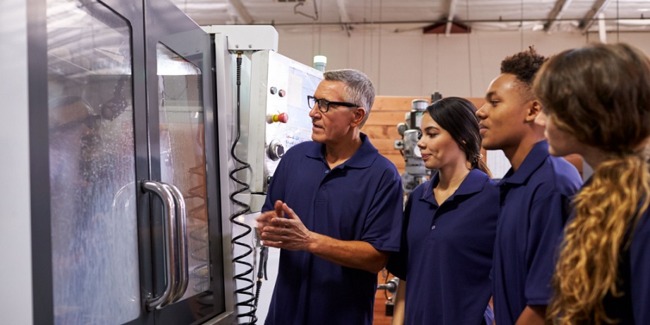 Apprentices wearing uniform being shown at a cabinet with glass doors with technology inside