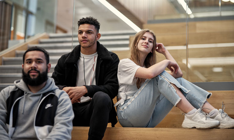 Three students sitting on the steps in The Hub.