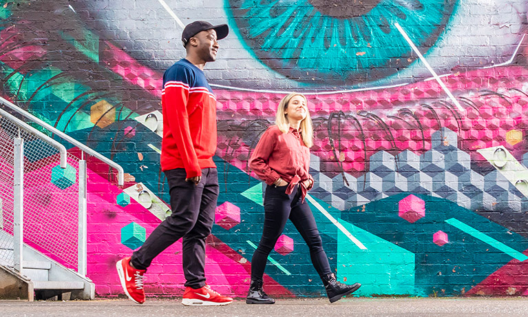 Two students walking past artwork on a wall