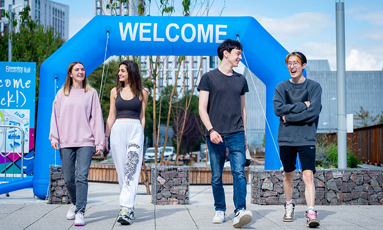 A group of students walking through an inflatable welcome sign on camp