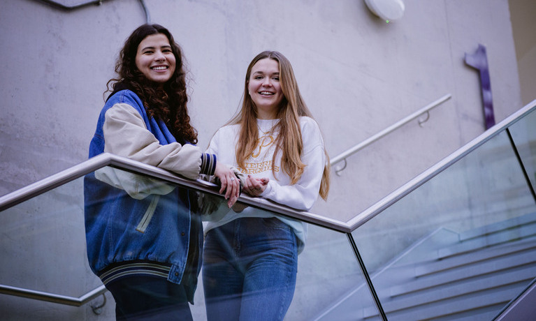 2 smiling females standing on an outside stairwell