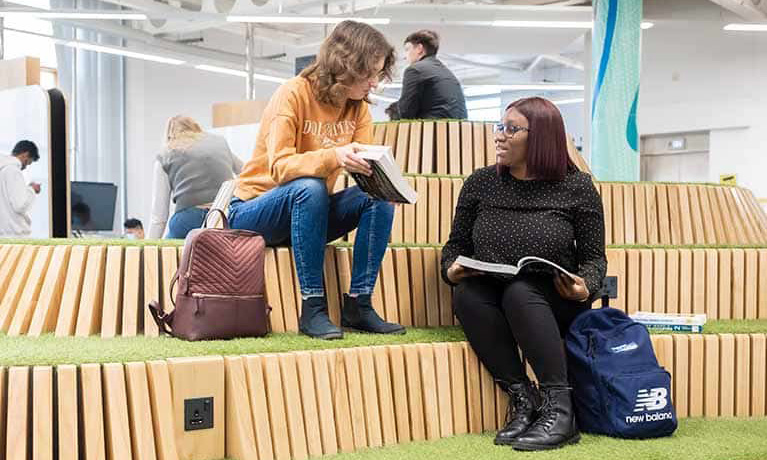 Two students sitting on grass seating in the library.