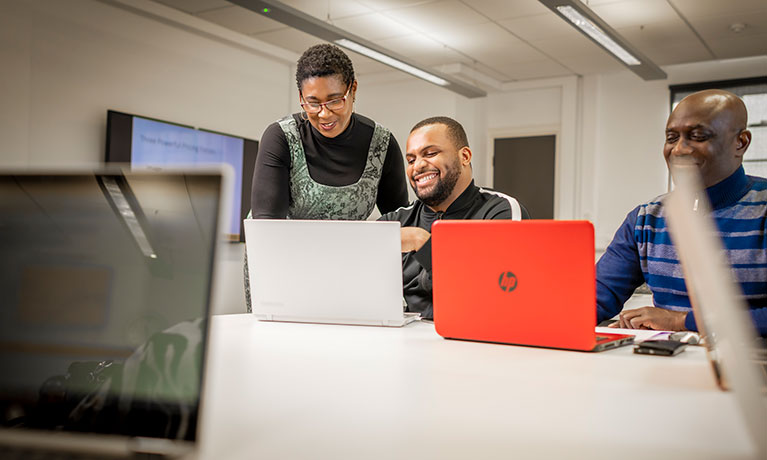 Lecturer stood over a students shoulder speaking to him whilst looking at a laptop screen