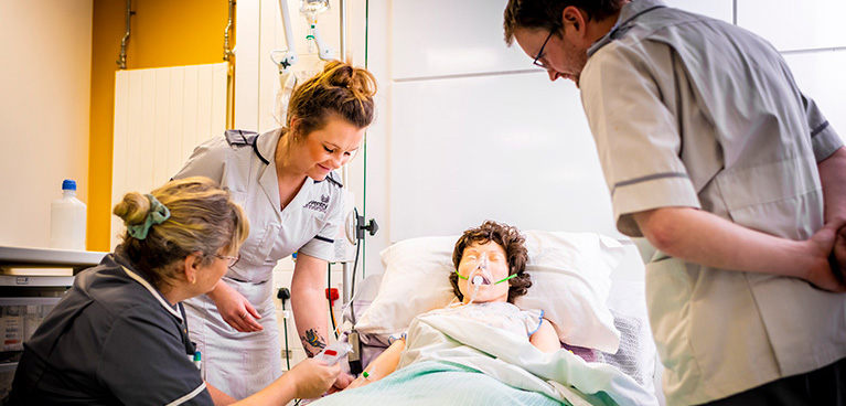 Students in the hospotal ward around a mannequin in a hospital bed