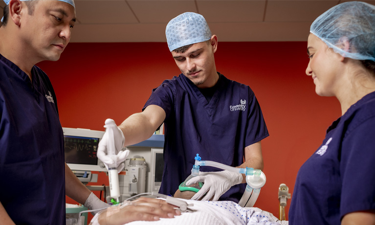 Three people in scrubs in a mock operating theatre