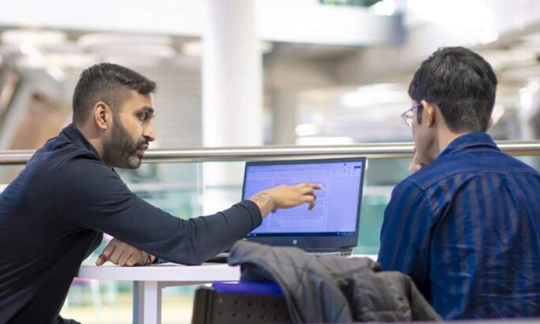 Member of staff sat next to a student pointing towards something on a laptop