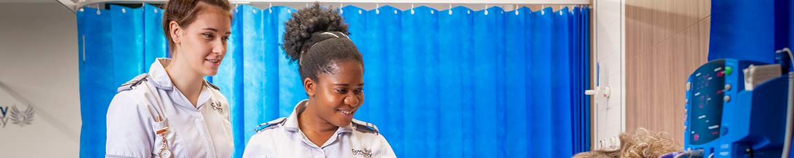 Two student nurses looking at patient on bed