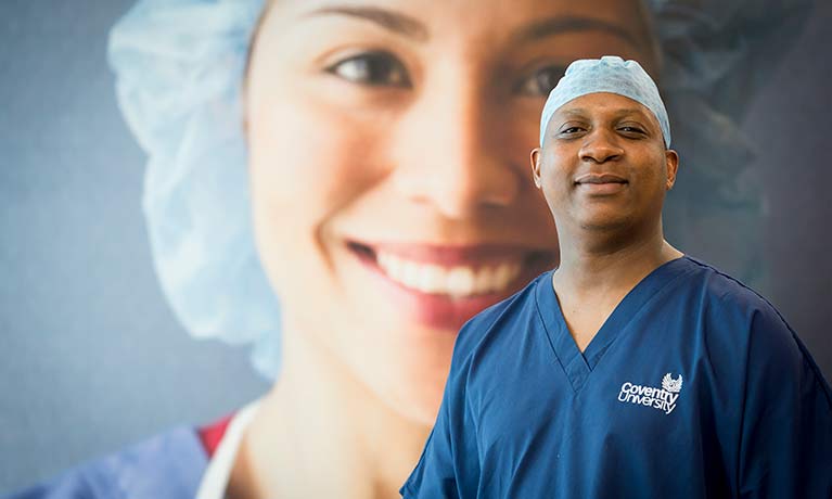 Male in scrubs looking at the camera with large face of female with hair covering on