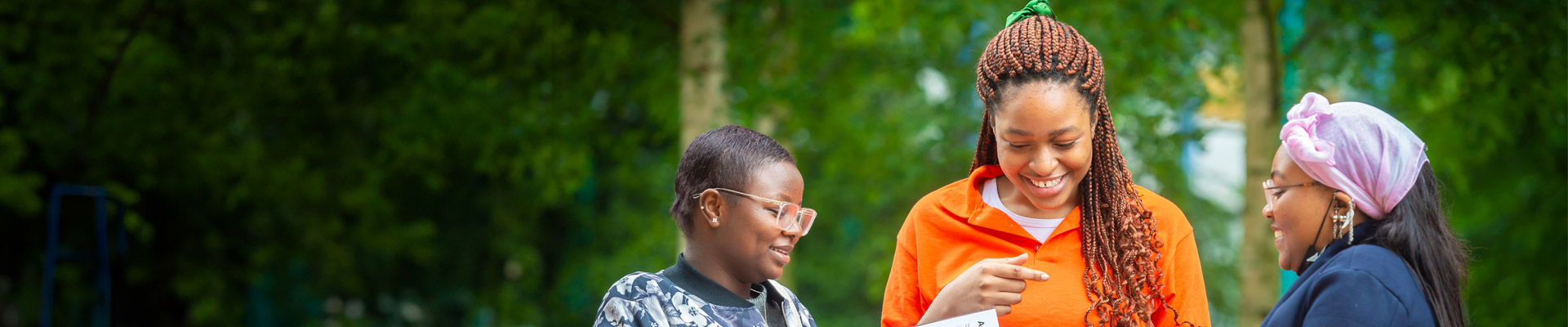 A prospective student in a bright orange top smiling with two older family members.