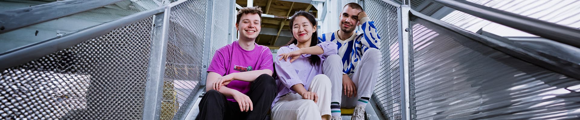 Three students sat on a staircase smiling
