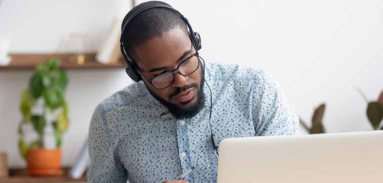 male student in front of a laptop wearing a headset