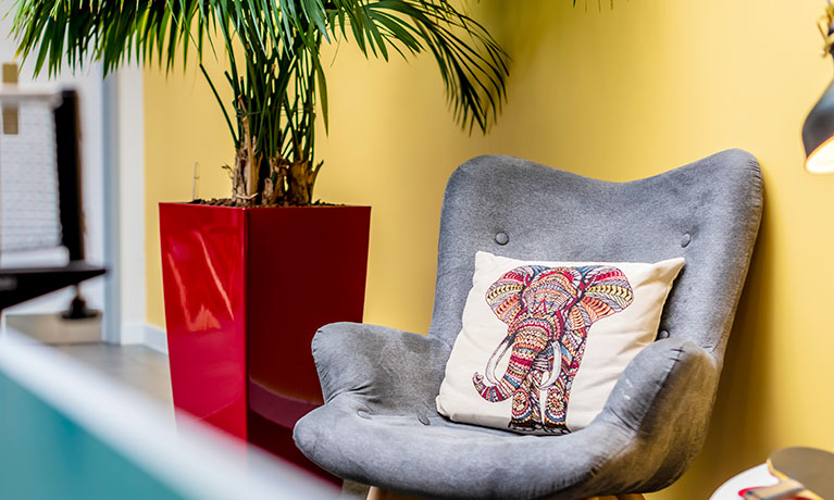 Grey chair with a cushion against a yellow wall