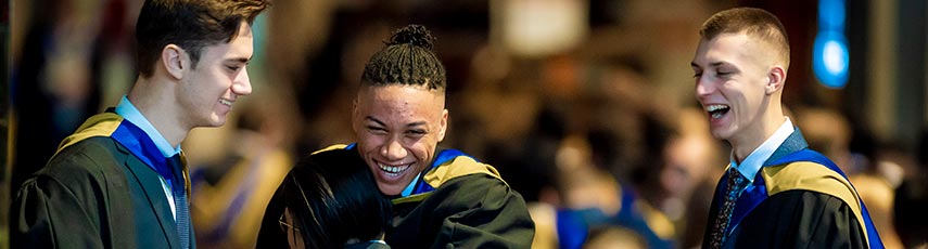 Three male students wearing graduation clothing smiling at each other