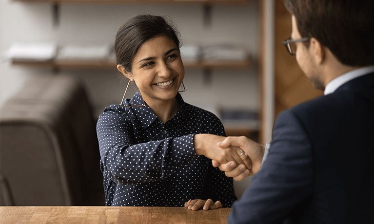 Two smartly dressed people smile at each other while shaking hands