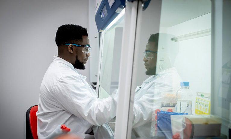 Male student in a lab coat using laboratory equipment to conduct scientific research.