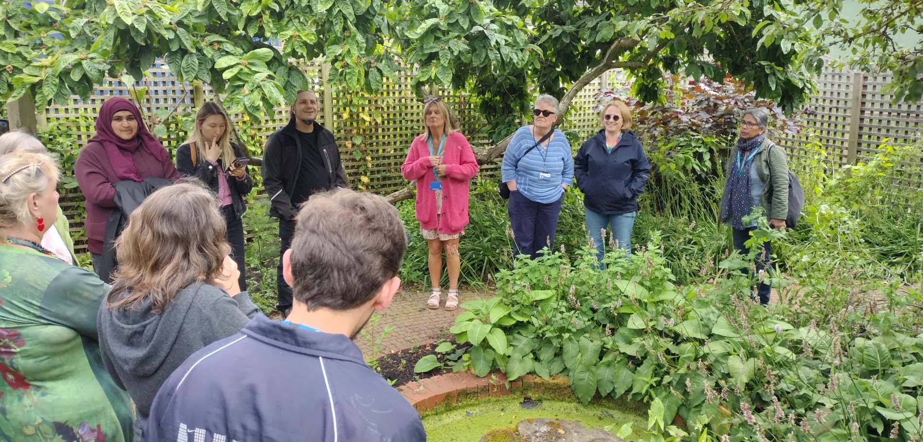 Various people gathered around a pond in a garden