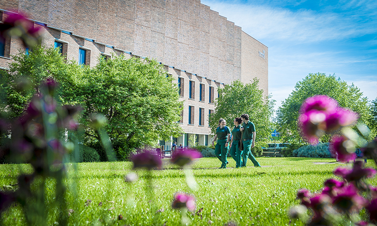 Building in the background and flowers and people walking past in the foreground