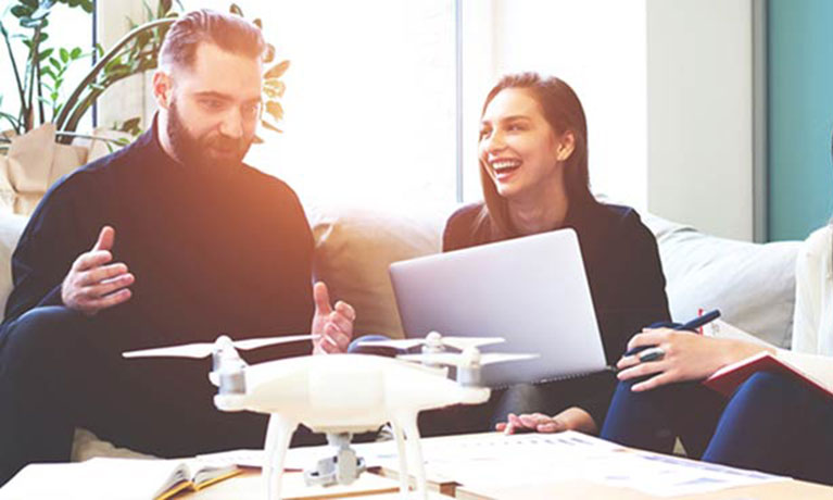 Male and female sat on sofa, looking at a model of a drone.