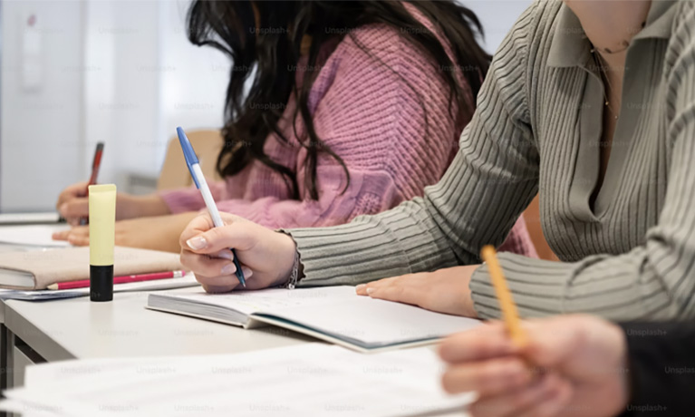 Close view of the hands of students writing in notebooks.