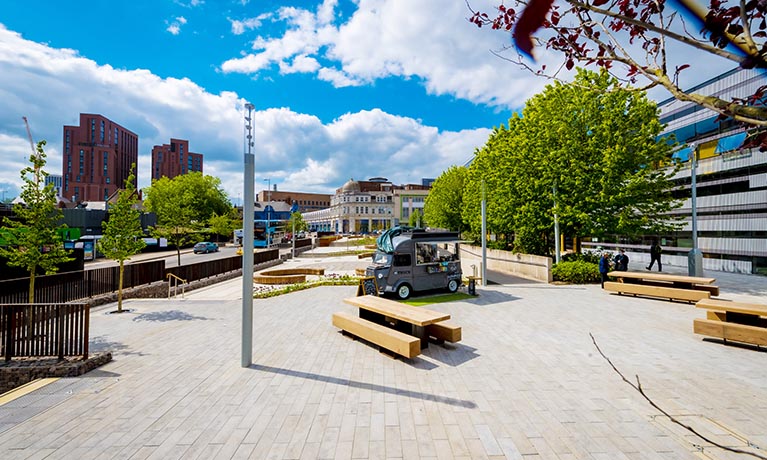 Starley Gardens next to The Hub on campus, with trees and seating areas.