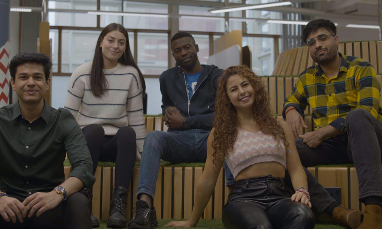 Five students sat down on benches in a campus building smiling