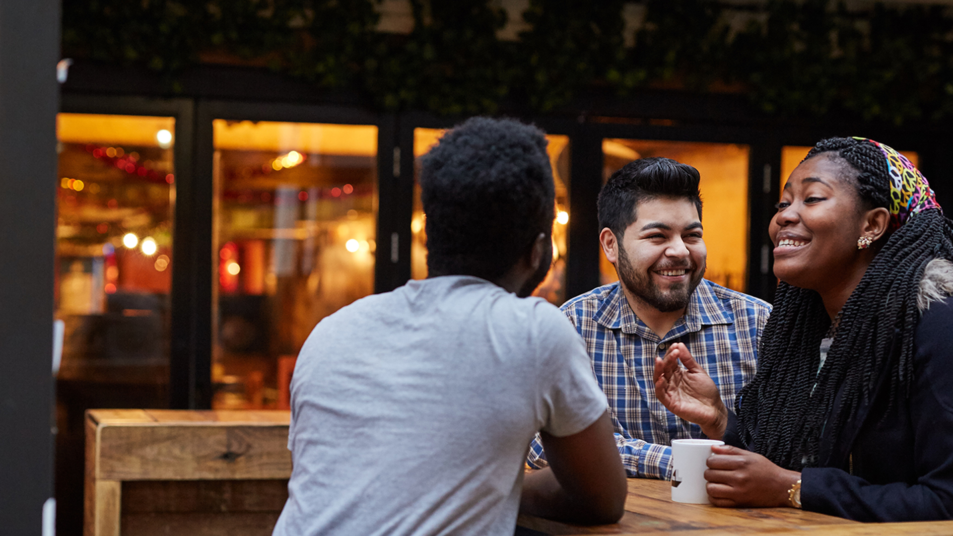 Three people standing at a tall table having coffee