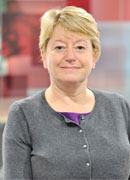 Short haired blonde adult woman wearing a grey top and smiling at the camera