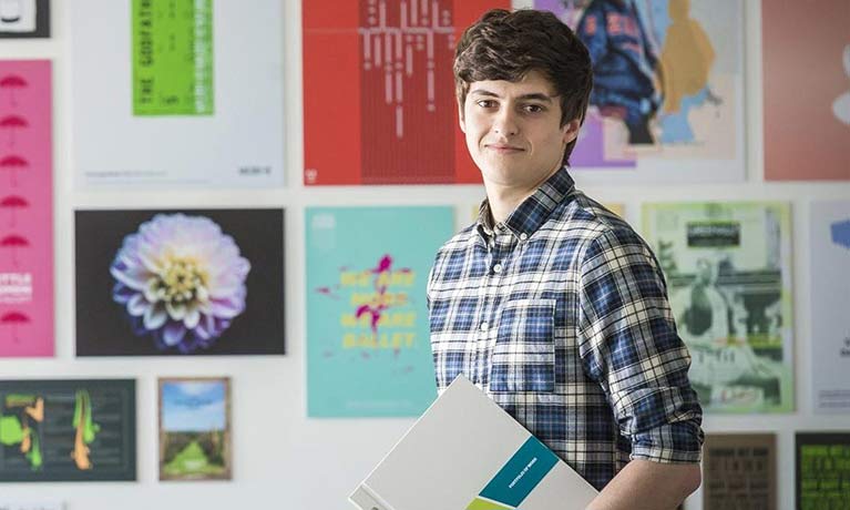 Smiling student standing in front of a wall covered in are