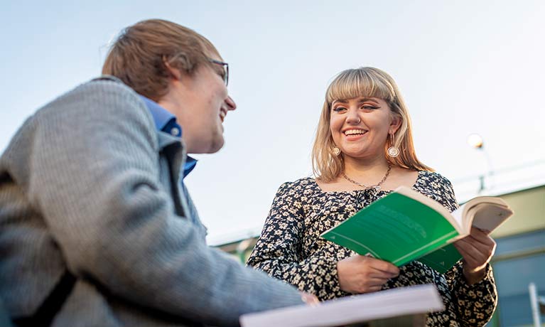 Two students holding books on campus