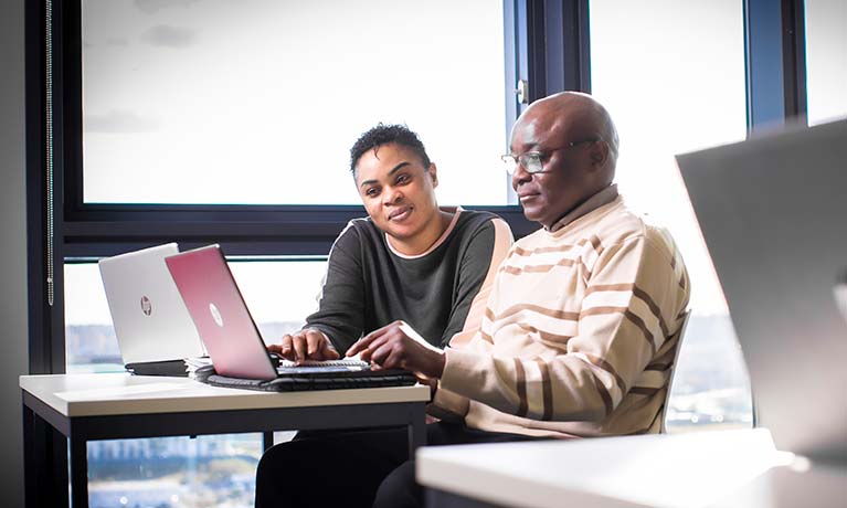 Two students sat at a desk working on a laptop