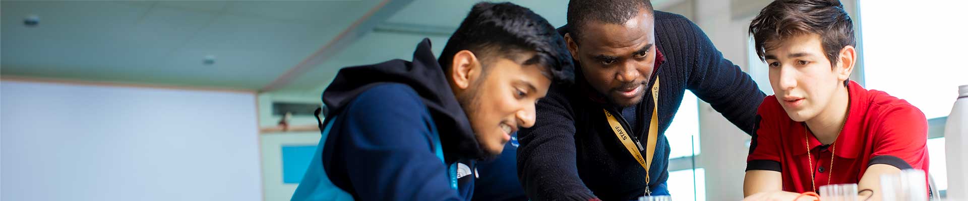 A male lecturer helping two male students with their work