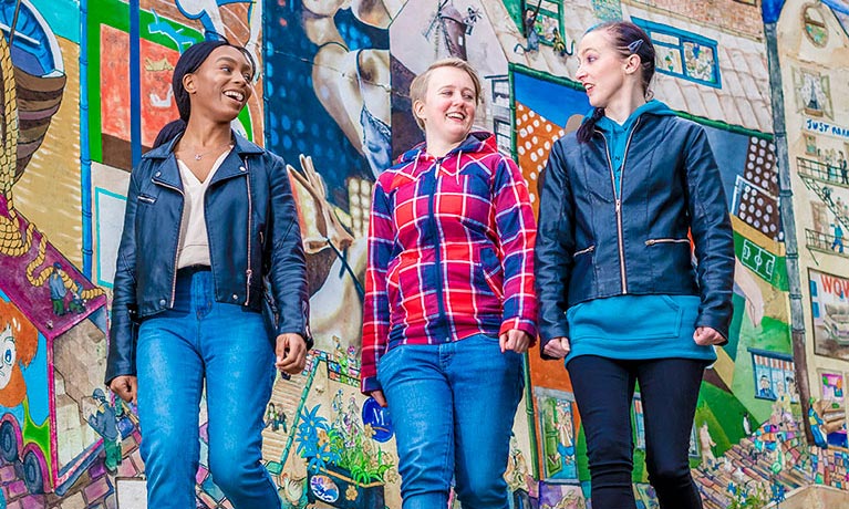 Students talking whilst walking past vibrant street art 