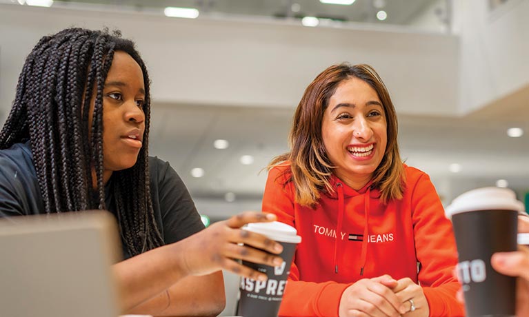 One student holding a coffee cup sat down talking to another student