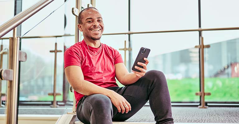 Male student sat down on steps holding a phone