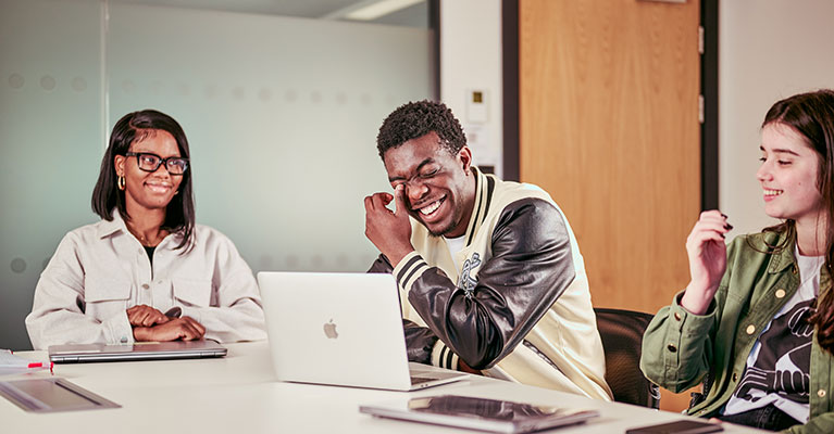 Group of students sat at a desk talking and laughing