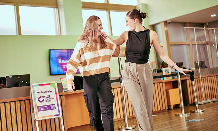 Two students laughing whilst walking through the CU Coventry building