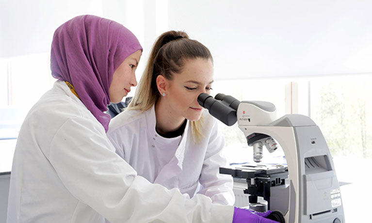 Two students wearing lab coats looking into a telescope