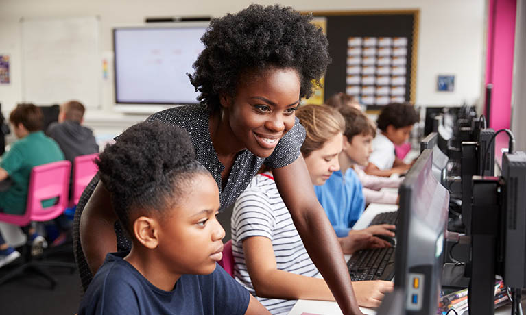 Female teacher looking at computer with pupil.