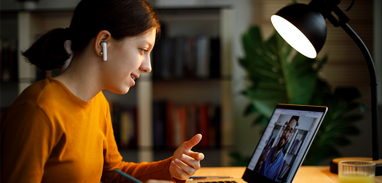 Woman sitting at a table talking into computer with earphones on